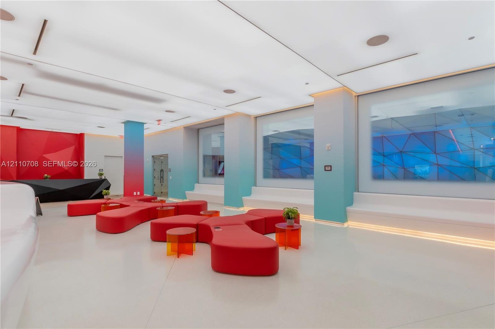 Expansive interior space featuring a geometric reception desk, integrated ambient cove lighting, recessed ceiling fixtures, built-in recessed seating benches, and gradient wall finishes Expansive interior space featuring a geometric reception desk, integrated ambient cove lighting, recessed ceiling fixtures, built-in recessed seating benches, and gradient wall finishes