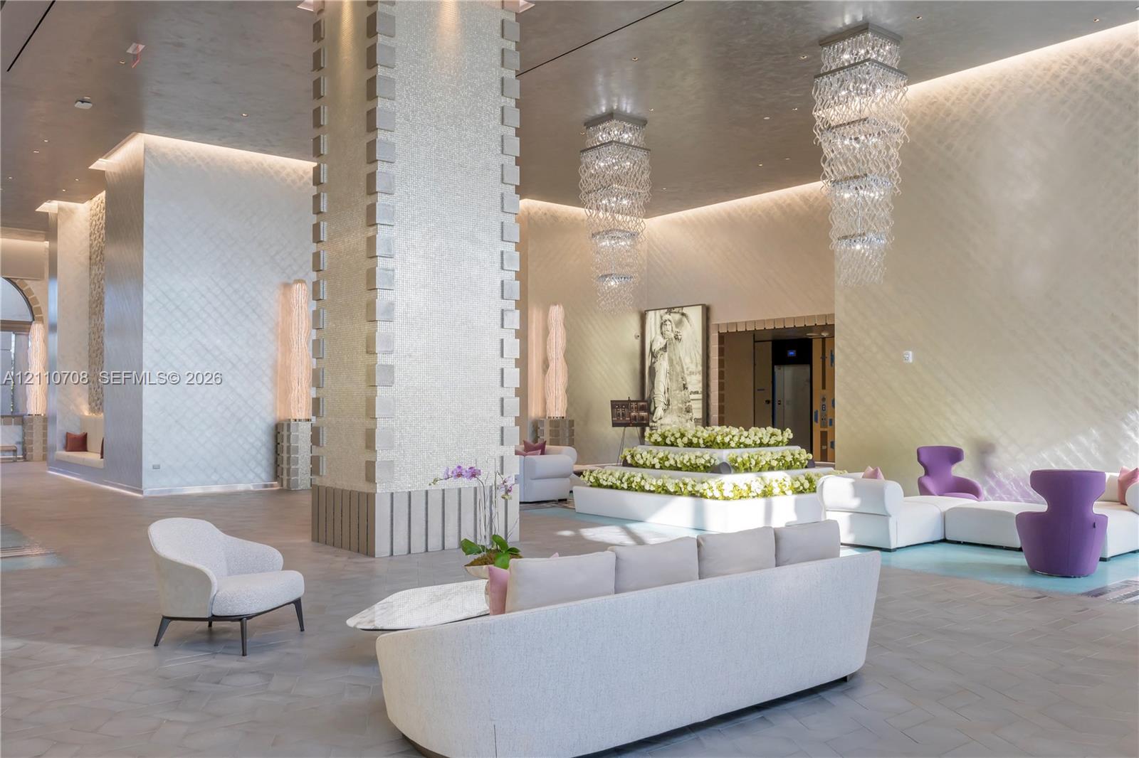 Expansive lobby featuring high ceilings with recessed lighting, tiered crystal chandeliers, textured wall finishes, and a structural column with decorative stone detailing Expansive lobby featuring high ceilings with recessed lighting, tiered crystal chandeliers, textured wall finishes, and a structural column with decorative stone detailing