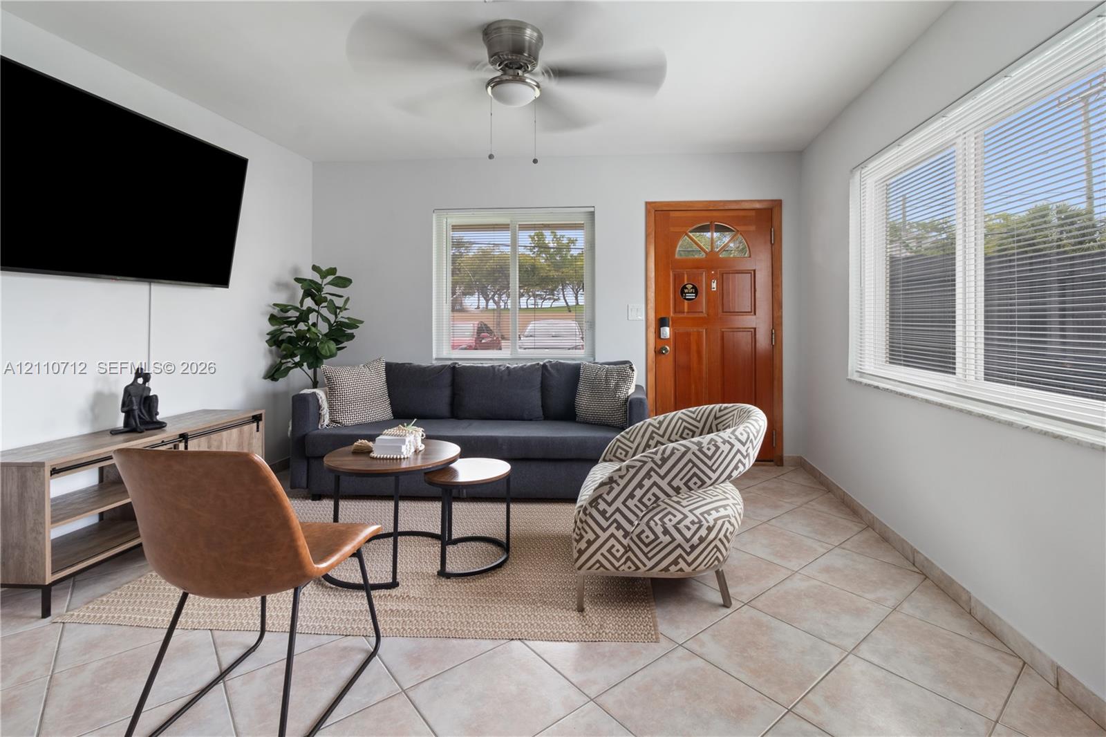 Living area featuring ceramic tile flooring, a multi-pane wood-finish entry door with an arched glass inset, dual large windows, and a ceiling-mounted fan