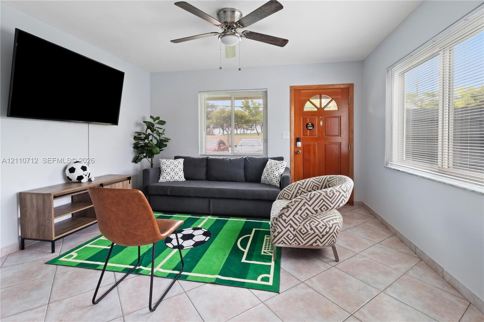Room featuring ceramic tile flooring, a central ceiling fan with integrated lighting, dual-pane windows, and a wood-finish exterior entry door