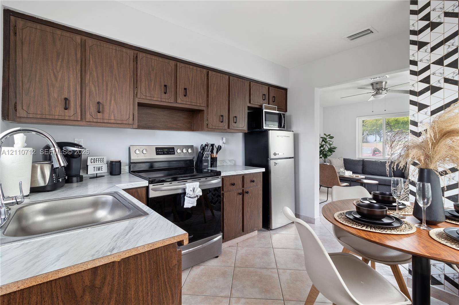 Kitchen featuring dark wood-finish cabinetry, stone-patterned laminate countertops, stainless steel appliances, and ceramic tile flooring