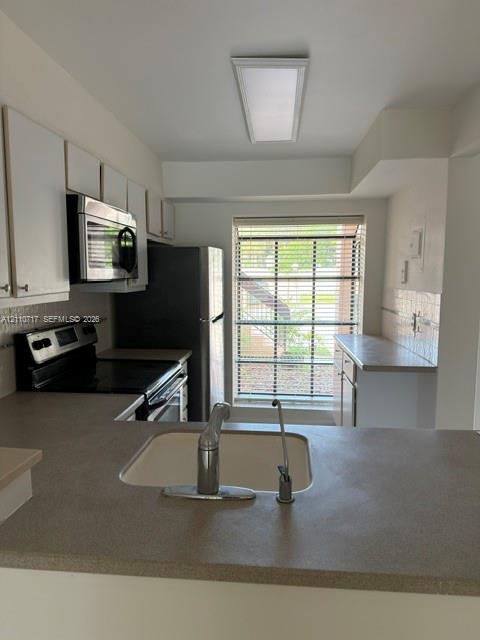 Kitchen featuring flat-panel white cabinetry, solid-surface countertops, integrated stainless steel appliances, and a rectangular window with horizontal blinds Kitchen featuring flat-panel white cabinetry, solid-surface countertops, integrated stainless steel appliances, and a rectangular window with horizontal blinds