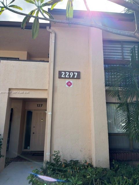 Stucco exterior facade featuring a covered entryway, private balcony with horizontal railings, and integrated address plaque Stucco exterior facade featuring a covered entryway, private balcony with horizontal railings, and integrated address plaque