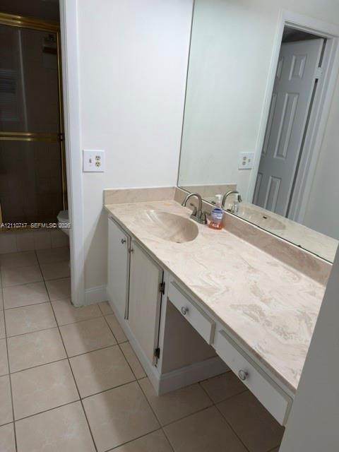 Vanity featuring a light-toned solid surface countertop with an integrated oval sink, full-width wall mirror, lower cabinetry, and ceramic tile flooring