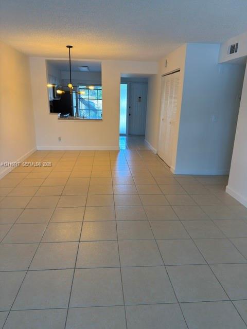 Open-concept area featuring neutral ceramic tile flooring, a multi-arm pendant light fixture, and a pass-through opening Open-concept area featuring neutral ceramic tile flooring, a multi-arm pendant light fixture, and a pass-through opening