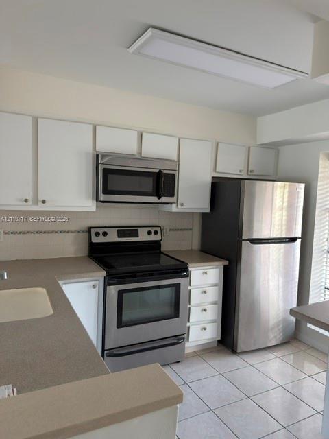 Kitchen featuring white cabinetry, solid-surface countertops, stainless steel appliances, ceramic tile flooring, and a recessed ceiling light fixture Kitchen featuring white cabinetry, solid-surface countertops, stainless steel appliances, ceramic tile flooring, and a recessed ceiling light fixture