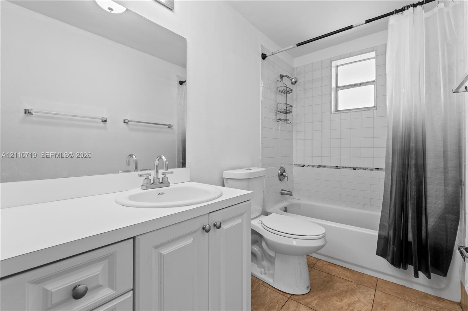 Bathroom featuring a white vanity with a solid surface countertop, an integrated sink, an expansive wall-mounted mirror, and a tub-shower combination with white wall tile