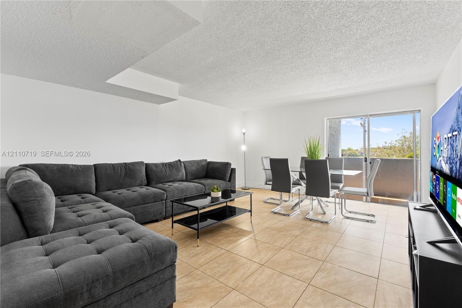 Living area featuring neutral tile flooring and sliding glass doors with access to an exterior balcony