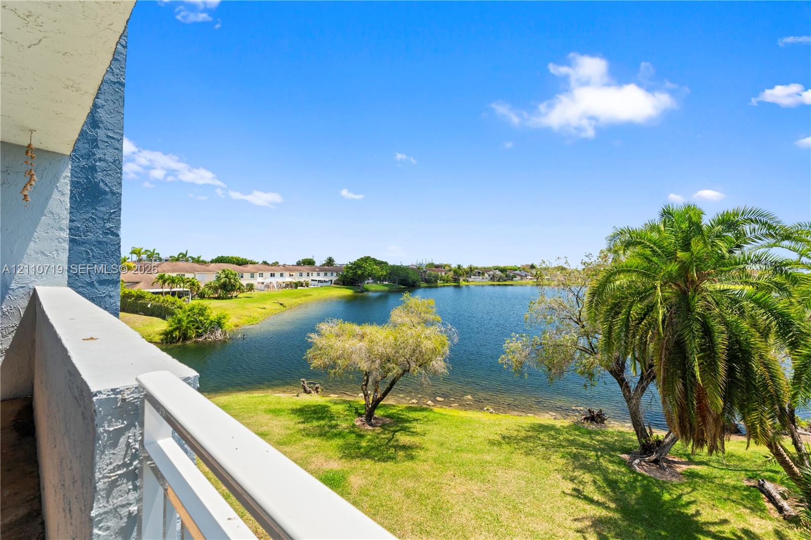 Elevated balcony featuring a white metal railing, overlooking a water feature with mature palm trees and landscaped grounds