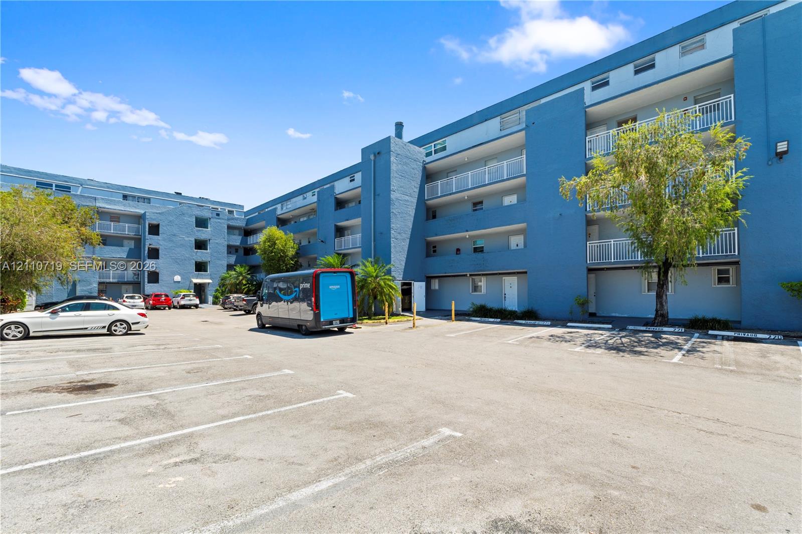 Multi-story residential building featuring painted masonry exterior, private balcony access, and an asphalt-paved surface parking lot