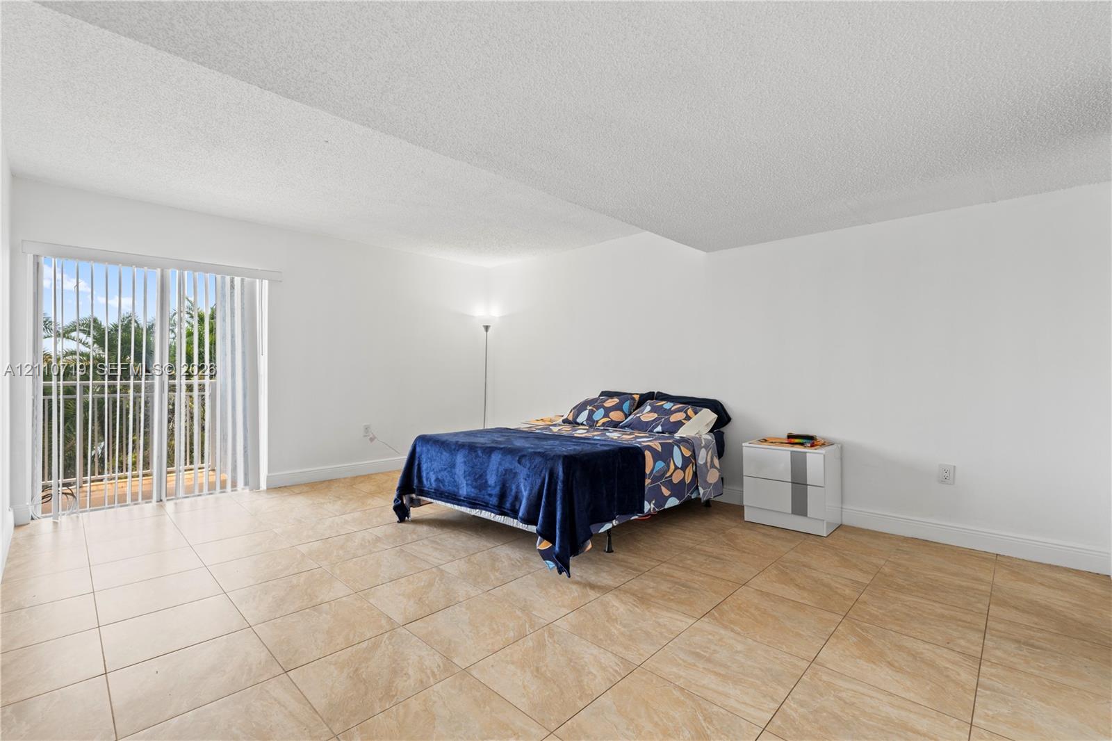 Neutral-tone tile flooring, expansive wall space, and sliding glass door with a white-finished frame