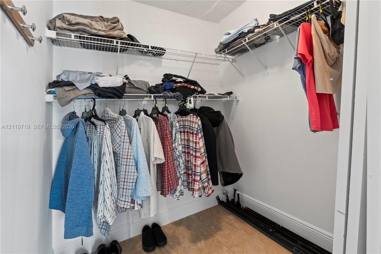 Walk-in closet featuring multi-level wire shelving systems and neutral floor tile