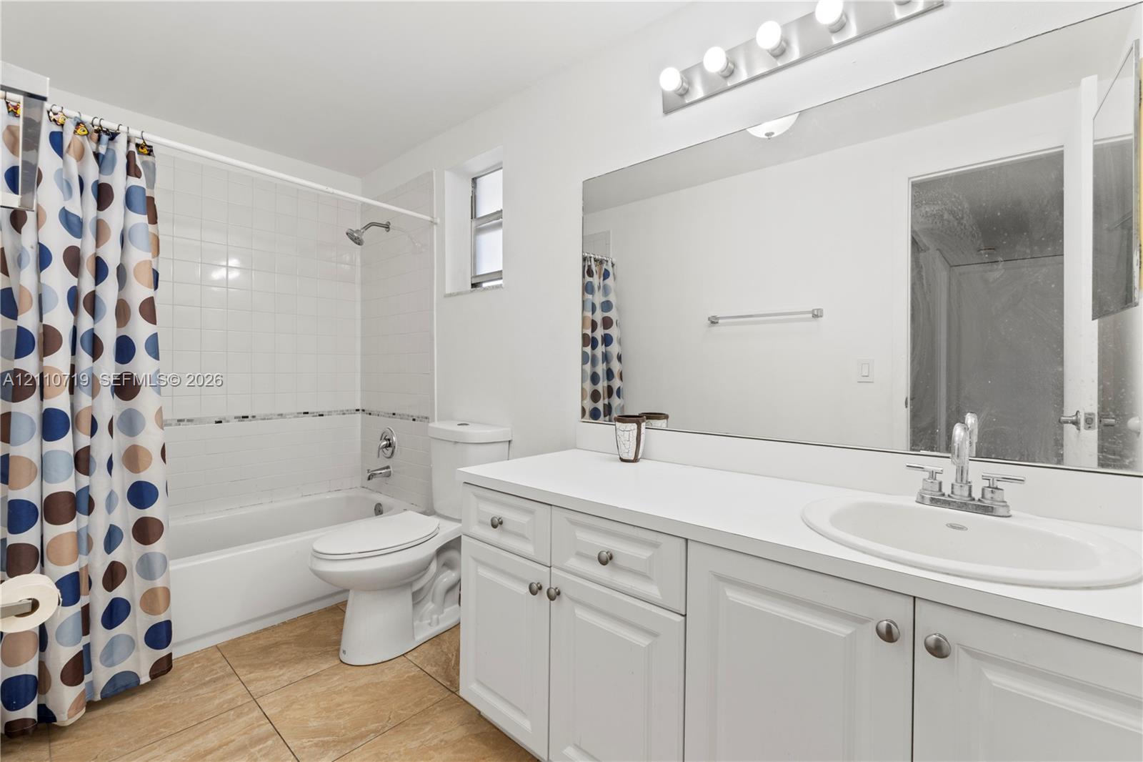 Bathroom featuring a white vanity cabinet with an integrated sink, polished chrome faucet, large vanity mirror, tile flooring, and a tub-shower combination with white wall tile
