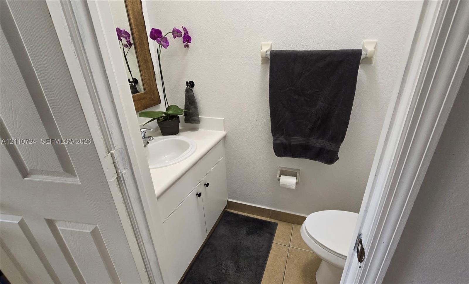 Powder room featuring a white vanity cabinet with a solid surface countertop, integrated sink, tile flooring, and wall-mounted hardware