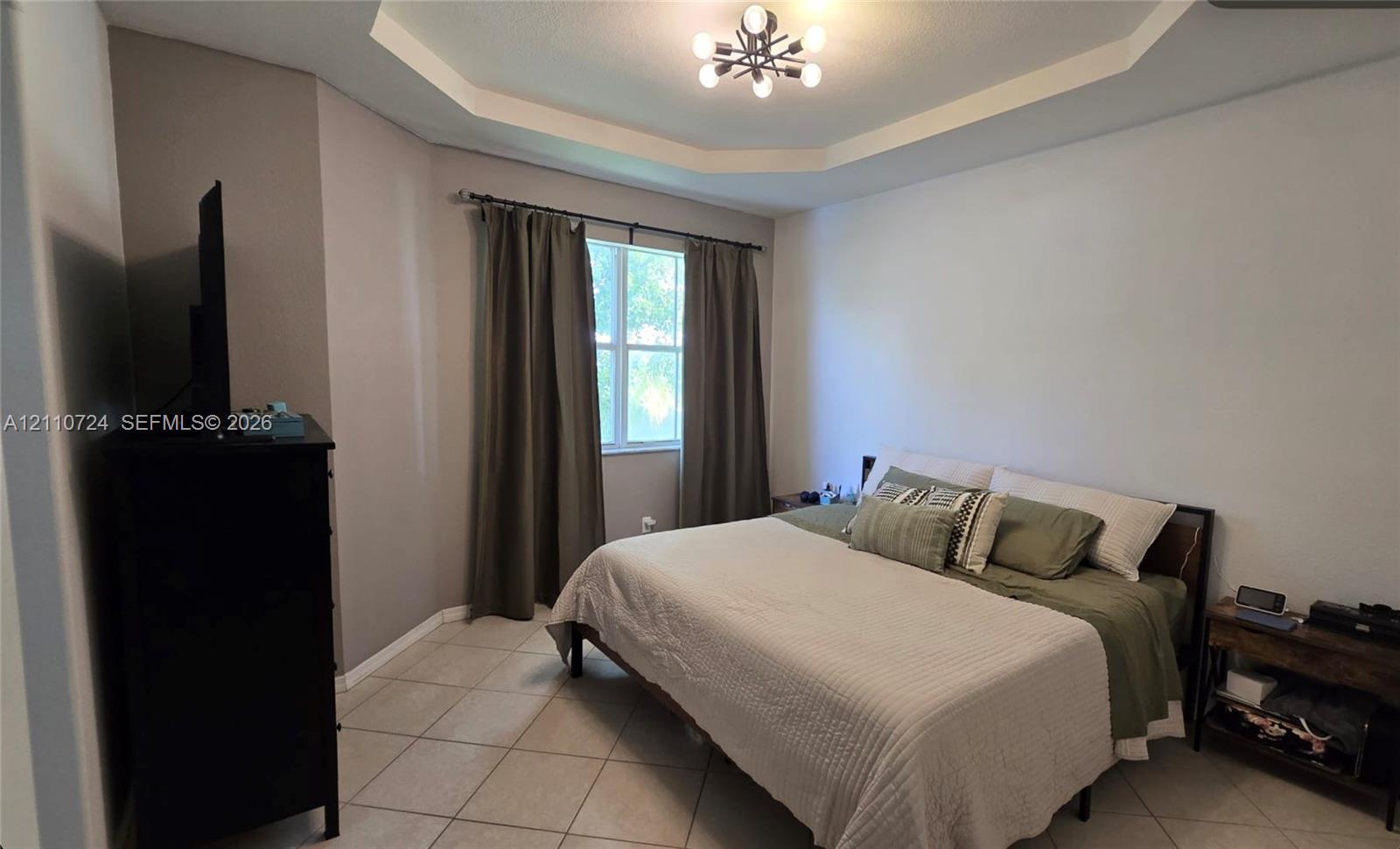 Tray ceiling featuring a multi-arm modern light fixture, neutral wall palette, and large-format tile flooring