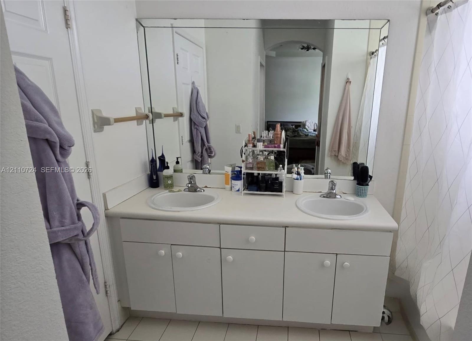 Dual-basin vanity featuring a solid surface countertop, white cabinetry with integrated hardware, and a large wall-mounted mirror