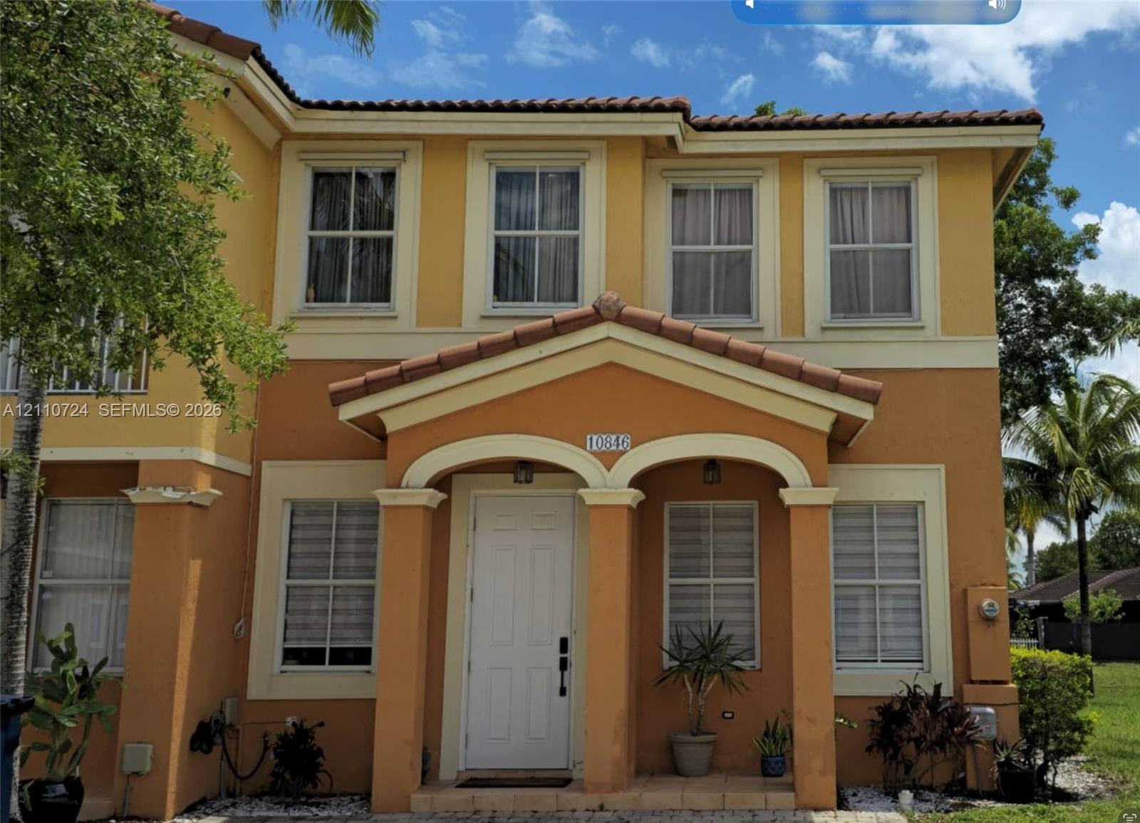 Two-story exterior featuring a stucco facade, covered entryway with arched portico, column supports, and a tile roof