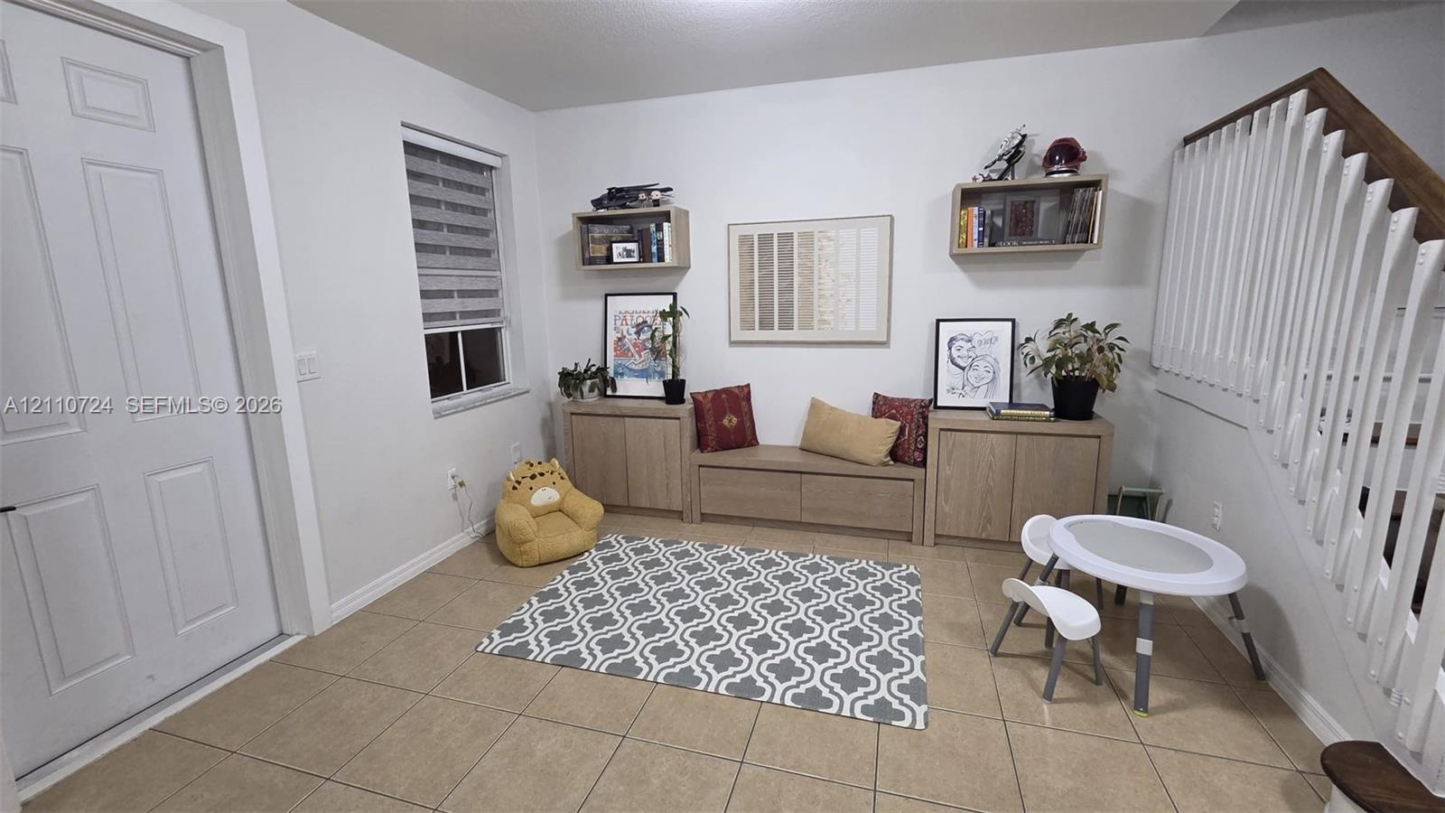 Neutral-toned tile flooring, built-in wooden cabinetry featuring a central bench seat, floating wall-mounted shelving, and a wooden staircase handrail