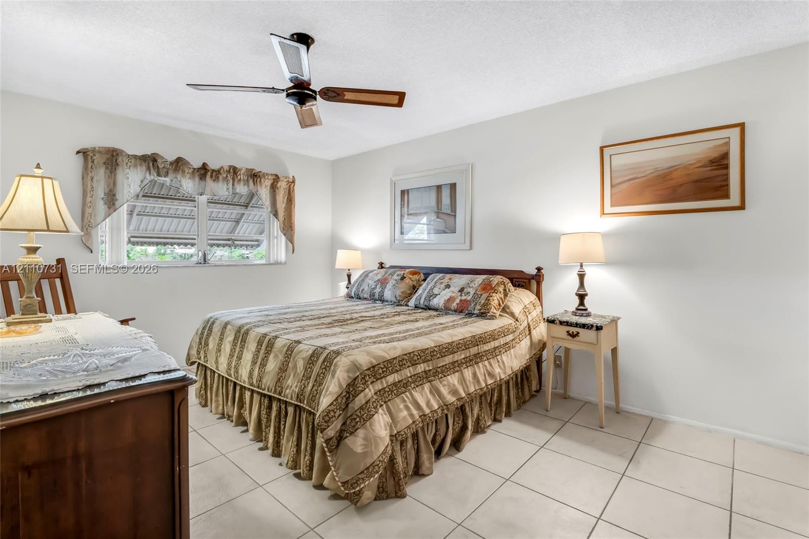 Neutral-toned room featuring large-format ceramic tile flooring, a multi-blade ceiling fan, and a horizontal window with a metal security awning