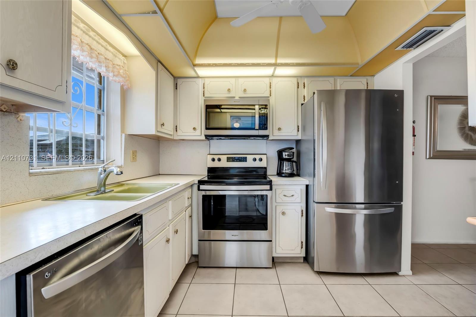 Kitchen featuring white cabinetry, stainless steel appliances, tile flooring, and a tray ceiling with integrated lighting