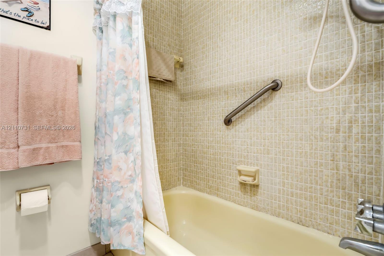 Bathtub featuring a neutral-toned basin, wall-mounted metal grab bar, built-in soap dish, and mosaic tile surround