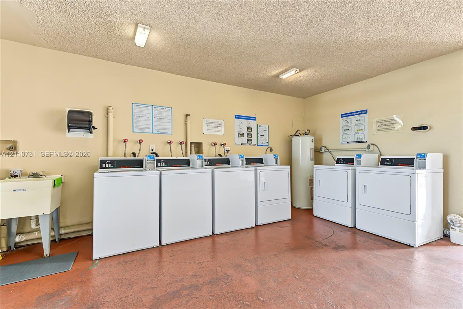 Laundry facility featuring multiple washer and dryer units, a utility sink, and a water heater