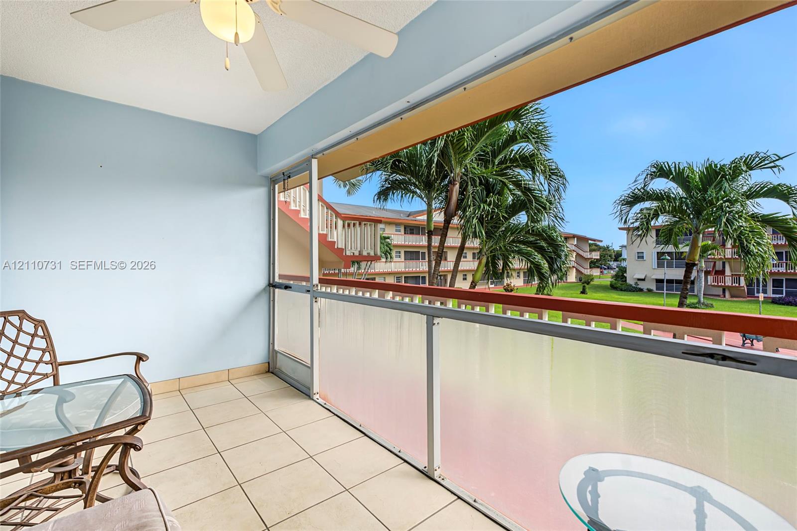 Covered balcony featuring tile flooring, a ceiling fan, and a glass-paneled railing