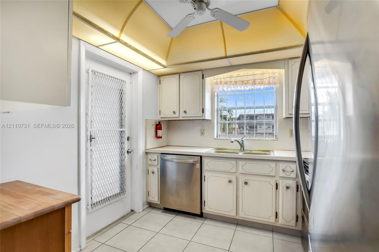 Kitchen featuring white cabinetry, stainless steel dishwasher, double-basin sink, tile flooring, and vaulted ceiling with recessed lighting