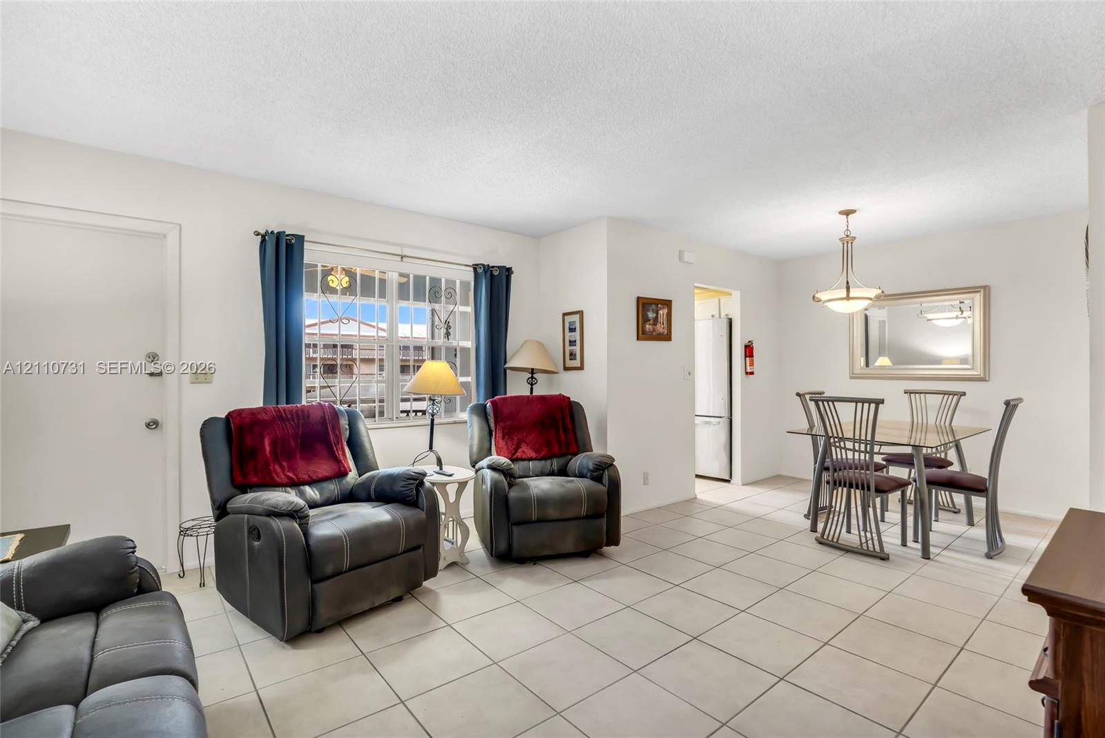 Open-concept living and dining area featuring ceramic tile flooring, multi-pane window with decorative security bars, and a multi-arm metal pendant light fixture