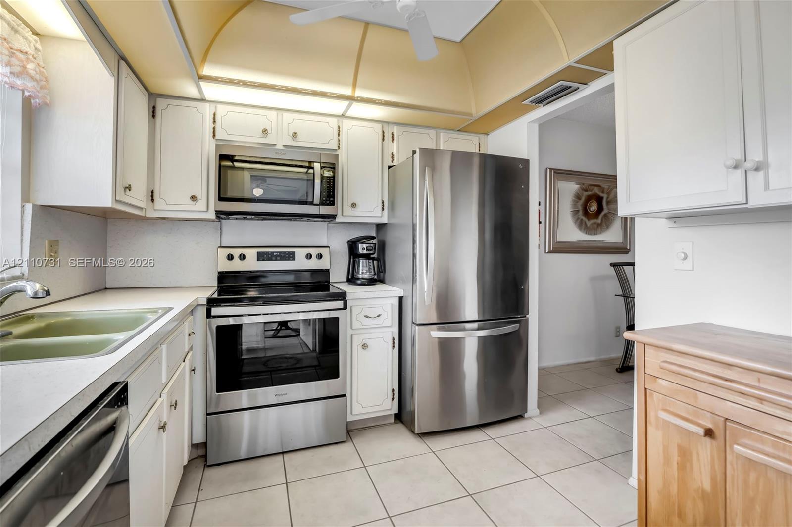 Kitchen featuring white cabinetry, stainless steel appliances, ceramic tile flooring, and integrated overhead soffit lighting