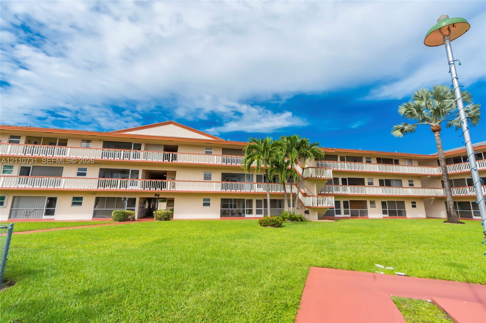 Three-story residential exterior featuring white balconies, a mansard roofline, and manicured green space
