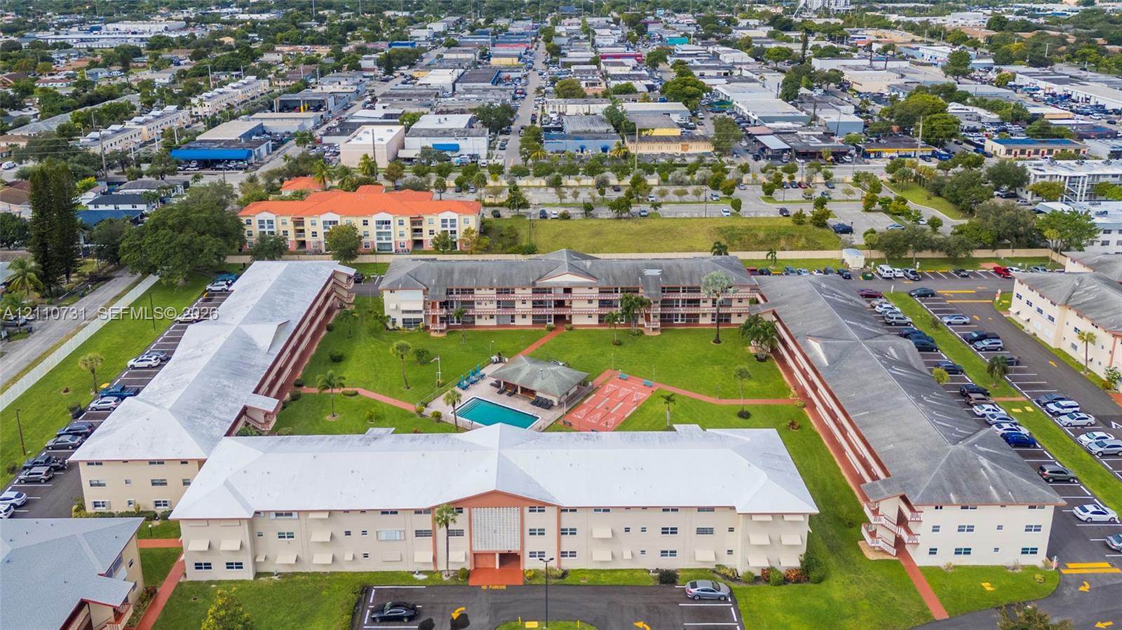 Multi-building complex featuring a central courtyard with an outdoor pool, paved walking paths, manicured landscaping, and designated surface parking