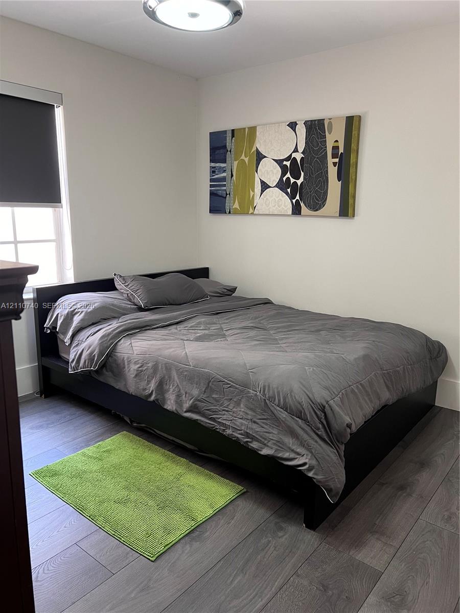 Room featuring wood-finish flooring, a multi-pane window with a roller shade, and a flush-mount overhead light fixture