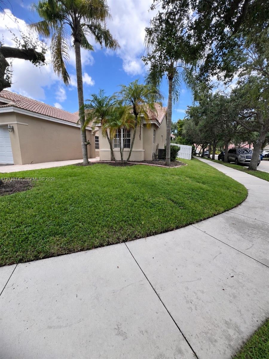 Single-story exterior featuring light-toned stucco siding, a tiled roof, mature palm trees, and a manicured lawn