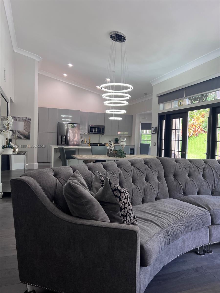 Open-concept interior featuring vaulted ceilings, modern multi-tier LED ring chandelier, dark wood-finish flooring, and floor-to-ceiling multi-panel glass doors