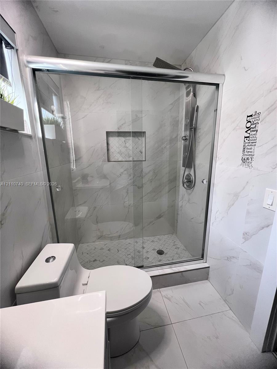 Walk-in shower featuring glass sliding doors, built-in recessed shelving, wall-mounted rain shower head, and floor-to-ceiling stone-finish tile surround