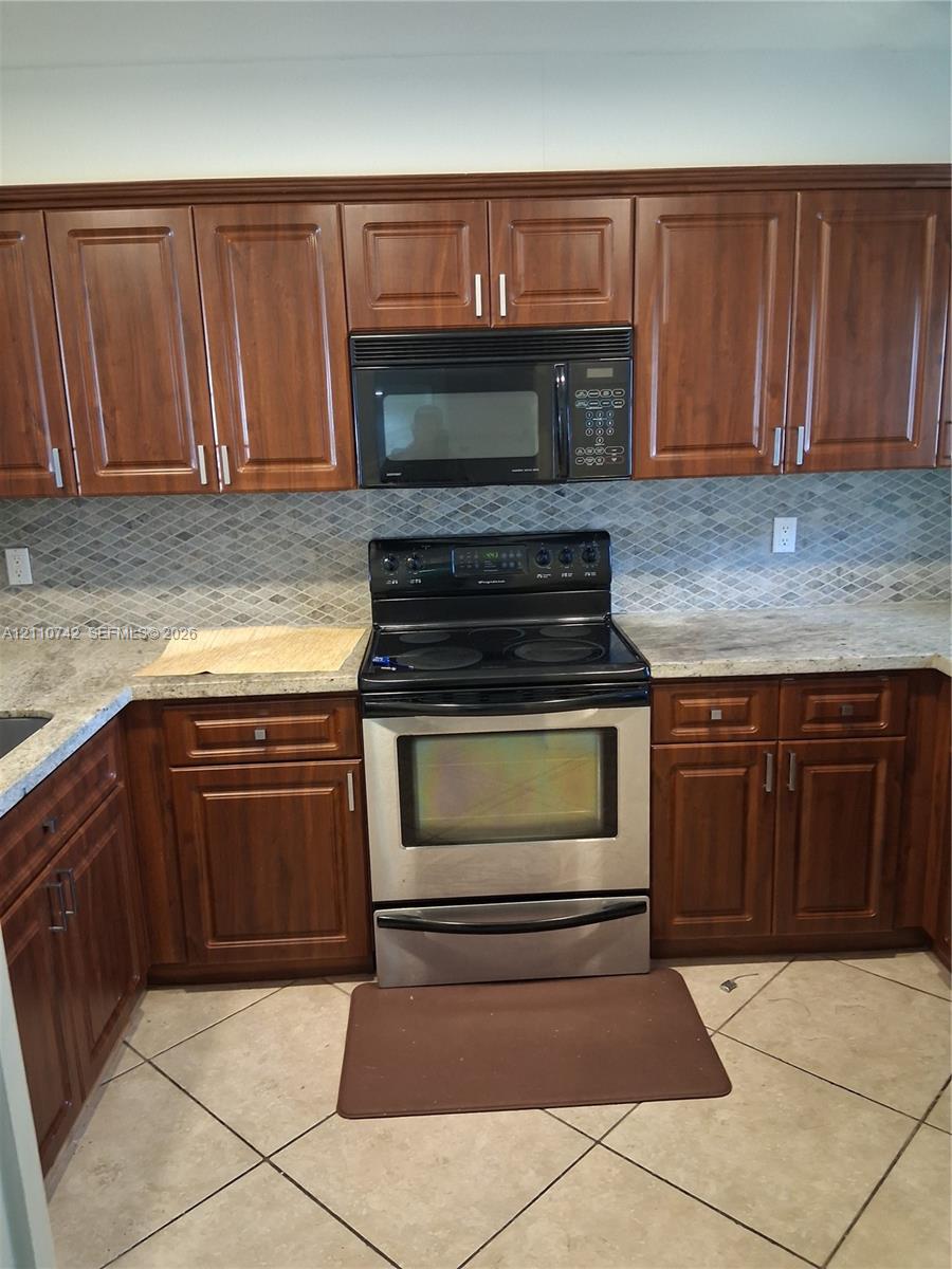Kitchen featuring dark wood-finish cabinetry, natural stone countertops, a mosaic tile backsplash, stainless steel electric range, and an integrated built-in microwave Kitchen featuring dark wood-finish cabinetry, natural stone countertops, a mosaic tile backsplash, stainless steel electric range, and an integrated built-in microwave
