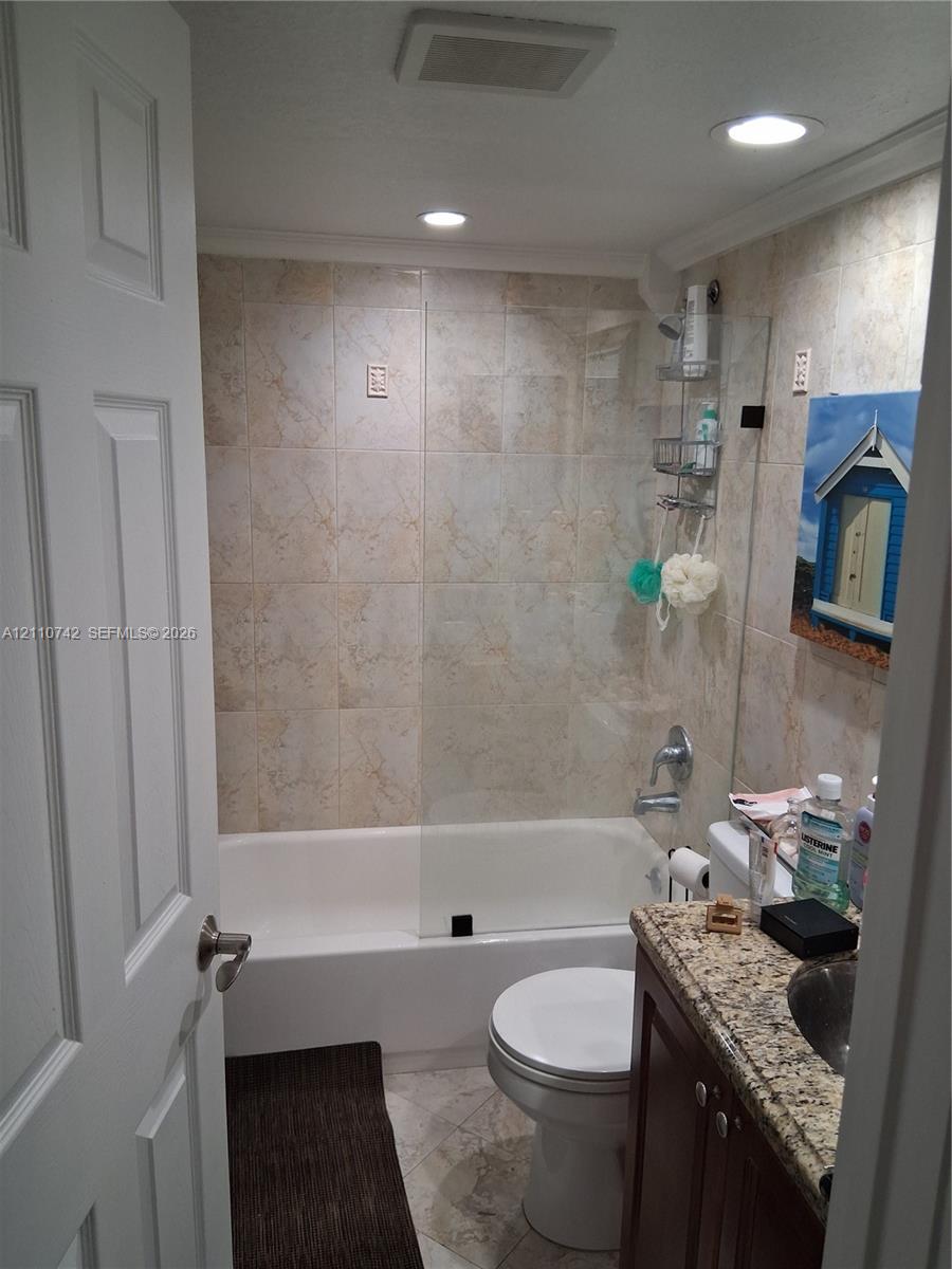 Full bathroom featuring a shower-tub combination with glass panel enclosure, tile-surround walls, stone-finish countertop, and recessed ceiling lighting Full bathroom featuring a shower-tub combination with glass panel enclosure, tile-surround walls, stone-finish countertop, and recessed ceiling lighting
