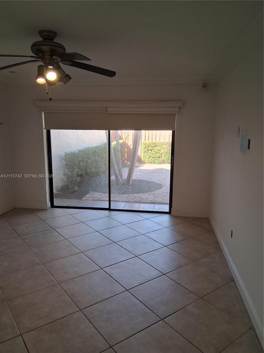 Neutral tile flooring, ceiling fan with integrated lighting, and sliding glass door opening to a paved patio area with mature landscaping Neutral tile flooring, ceiling fan with integrated lighting, and sliding glass door opening to a paved patio area with mature landscaping