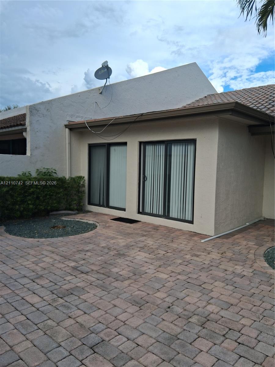 Exterior patio featuring stone paver flooring, stucco wall finish, tiled roofing, and dual sliding glass doors