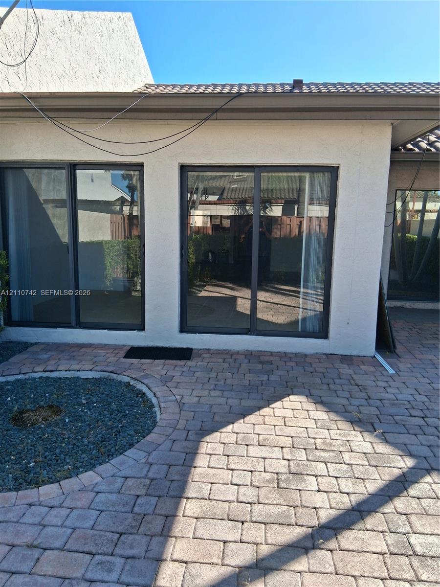 Stucco exterior featuring dual sliding glass doors, paver patio, and circular gravel garden bed