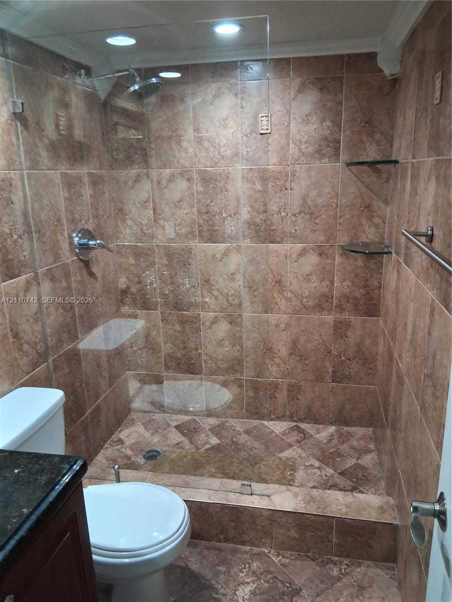 Walk-in shower featuring brown stone-finish wall and floor tile, glass panel enclosure, built-in glass shelving, and chrome-finish shower fixture Walk-in shower featuring brown stone-finish wall and floor tile, glass panel enclosure, built-in glass shelving, and chrome-finish shower fixture