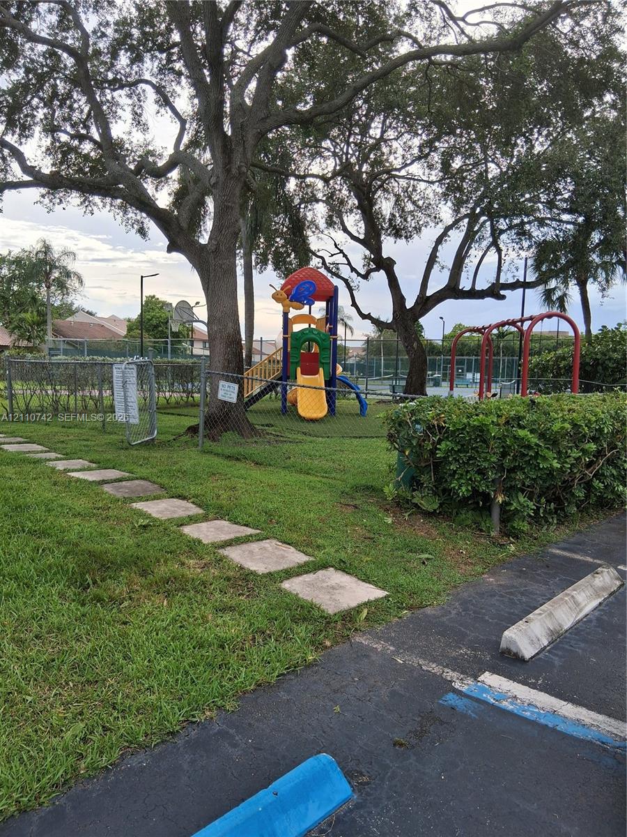 Community recreation area featuring a fenced playground, paved walkways, mature shade trees, and perimeter landscaping Community recreation area featuring a fenced playground, paved walkways, mature shade trees, and perimeter landscaping