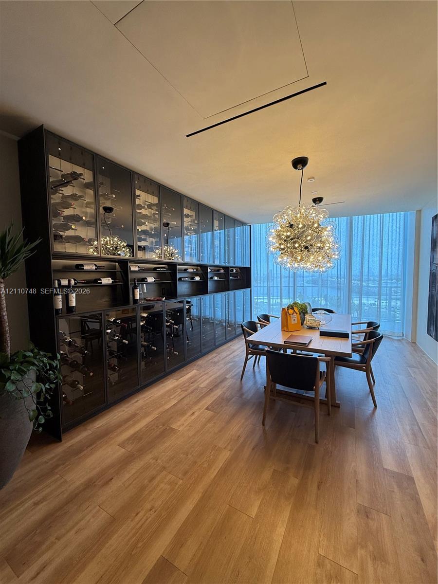 Floor-to-ceiling custom wine storage with glass-panel cabinetry, wood-finish flooring, statement globe chandelier, and expansive windows
