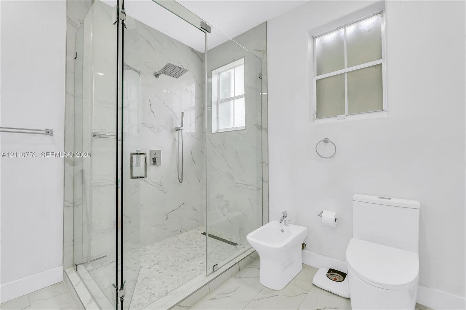Walk-in shower with floor-to-ceiling stone-finish tile, glass enclosure, and rainfall showerhead, complemented by a bidet and dual-flush toilet