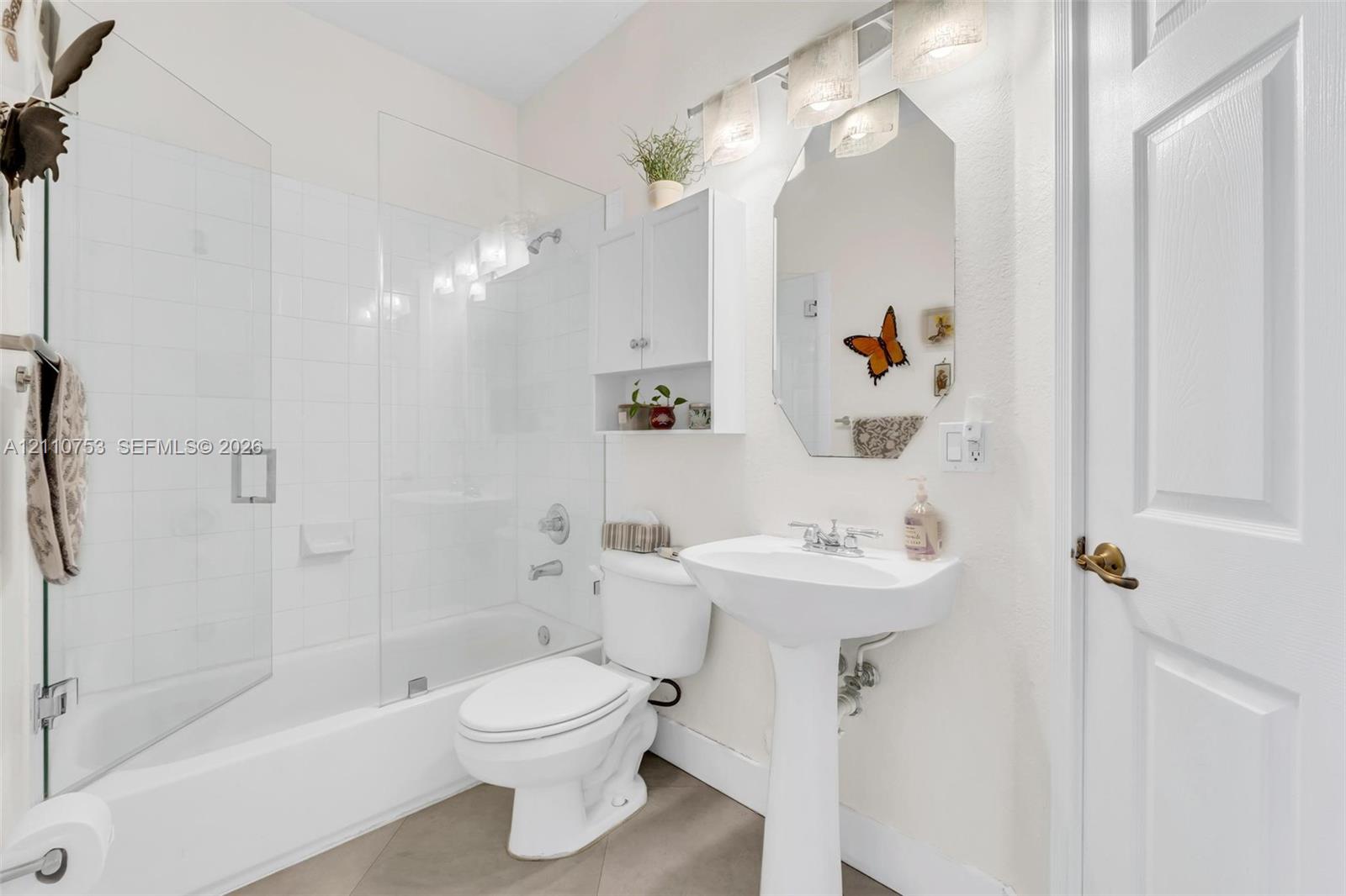 Bathroom featuring a glass-enclosed shower and tub combination, pedestal sink, wall-mounted medicine cabinet, and three-light vanity fixture