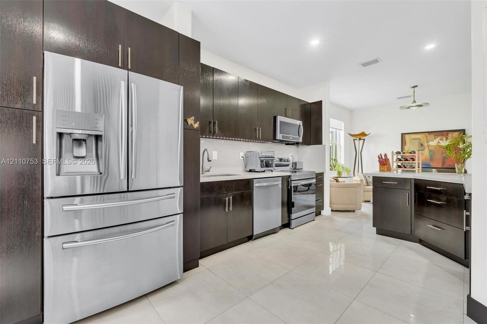 Kitchen featuring dark wood-finish cabinetry, stainless steel appliances, a peninsula with stone-finish countertop, and tile flooring