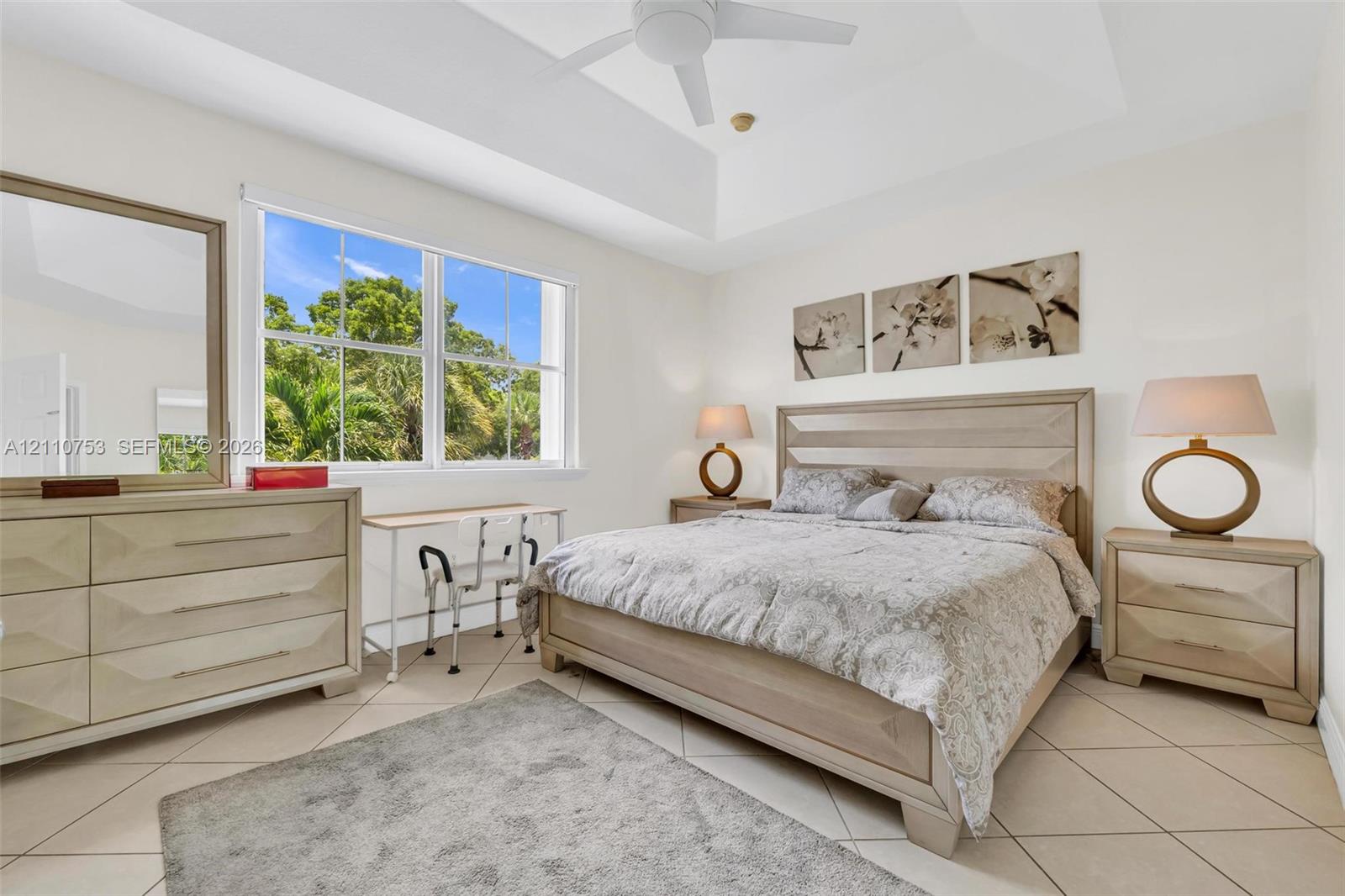 Tray ceiling featuring a central ceiling fan, large windows, and tile flooring