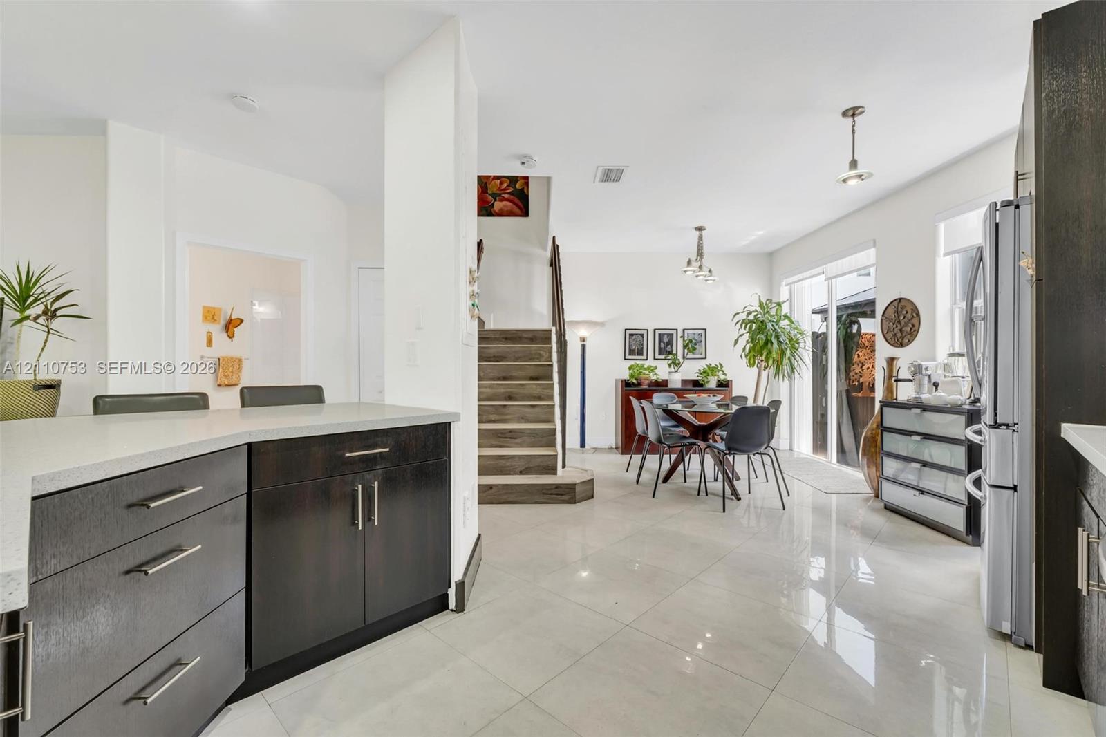 Kitchen featuring dark-finish cabinetry, quartz countertops, and polished tile flooring, with wood-finish stairs and sliding glass doors