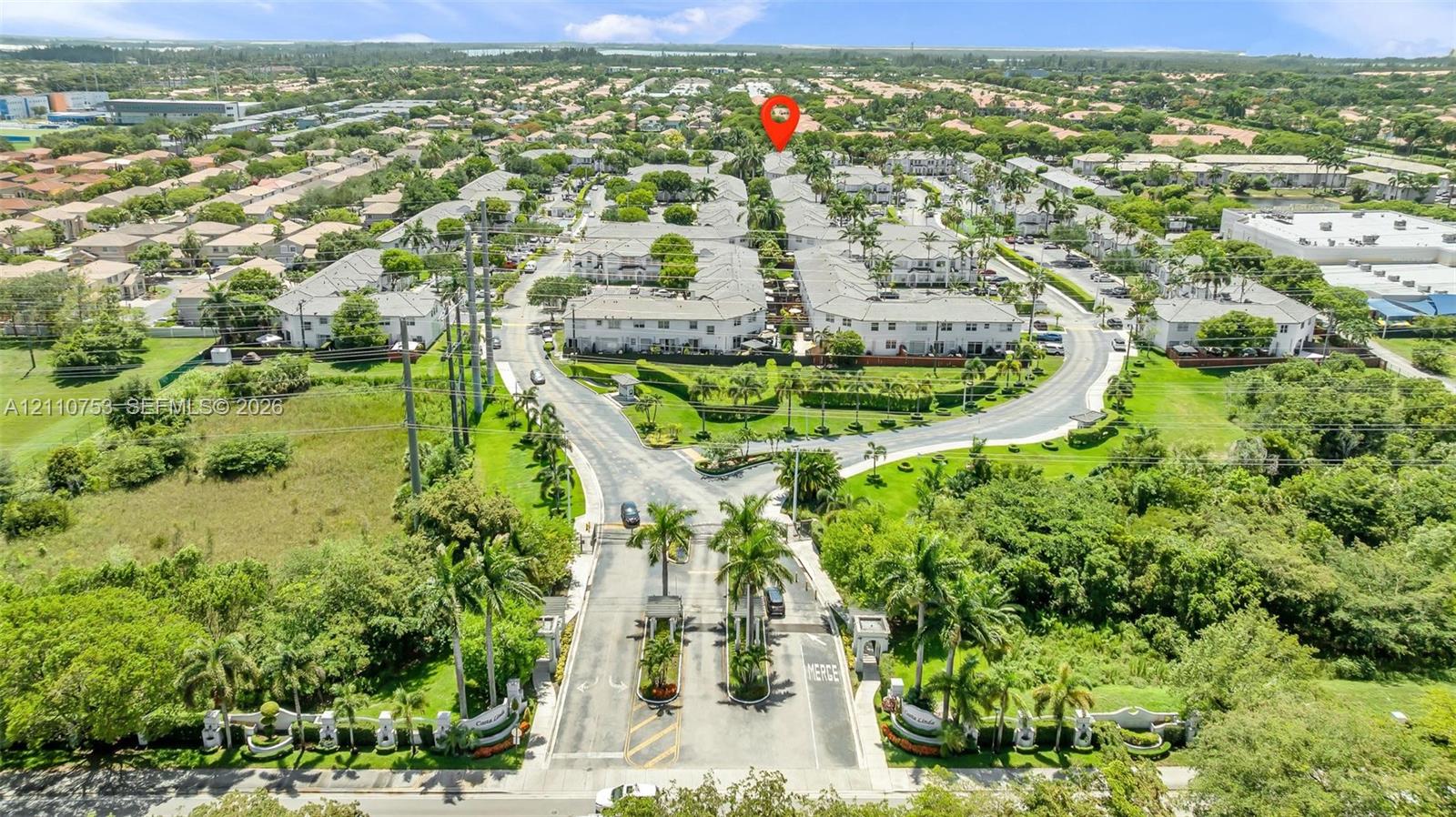 Aerial perspective of a gated community featuring paved roadways, manicured landscaping, mature palm trees, and multi-unit residential structures